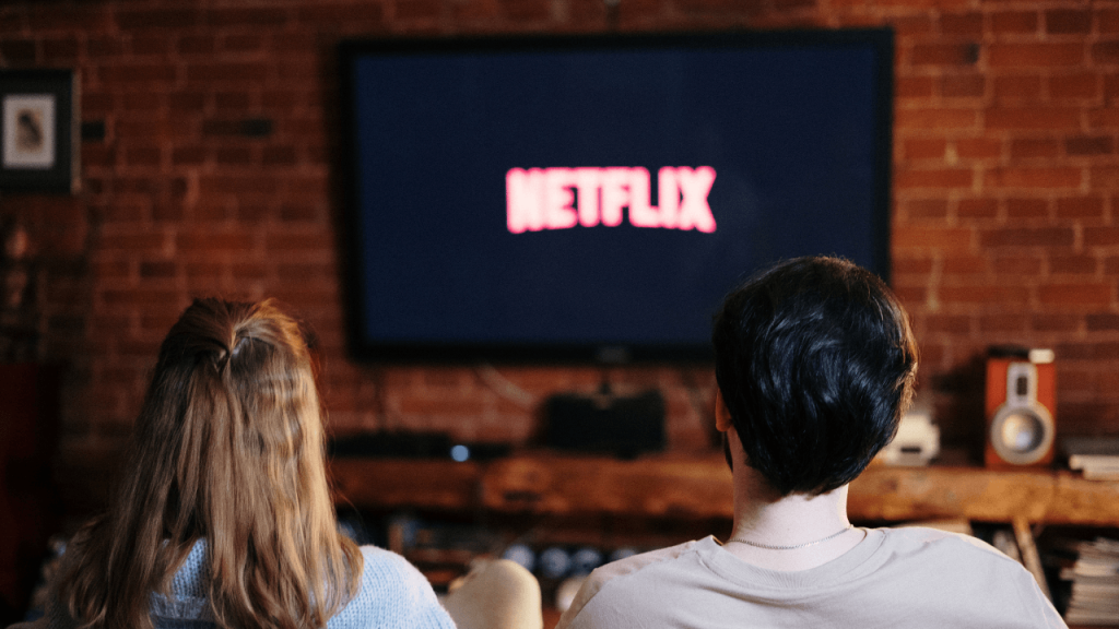 Immagine di un televisore con la scritta NETFLIX e due persone sedute su un divano che lo guardano.