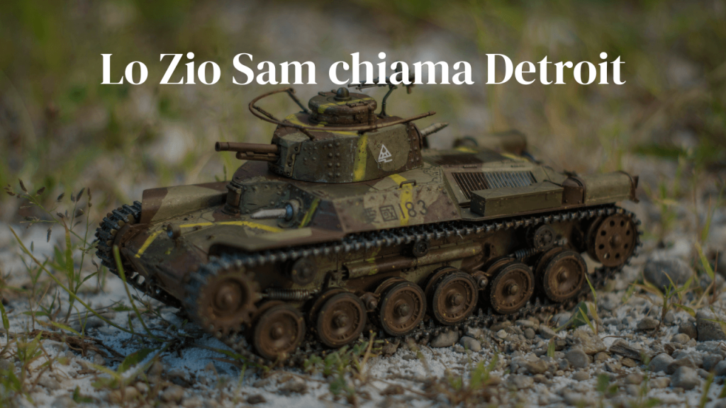 Modellino di carro armato in mimetica su ghiaia, con vegetazione sfocata sullo sfondo.